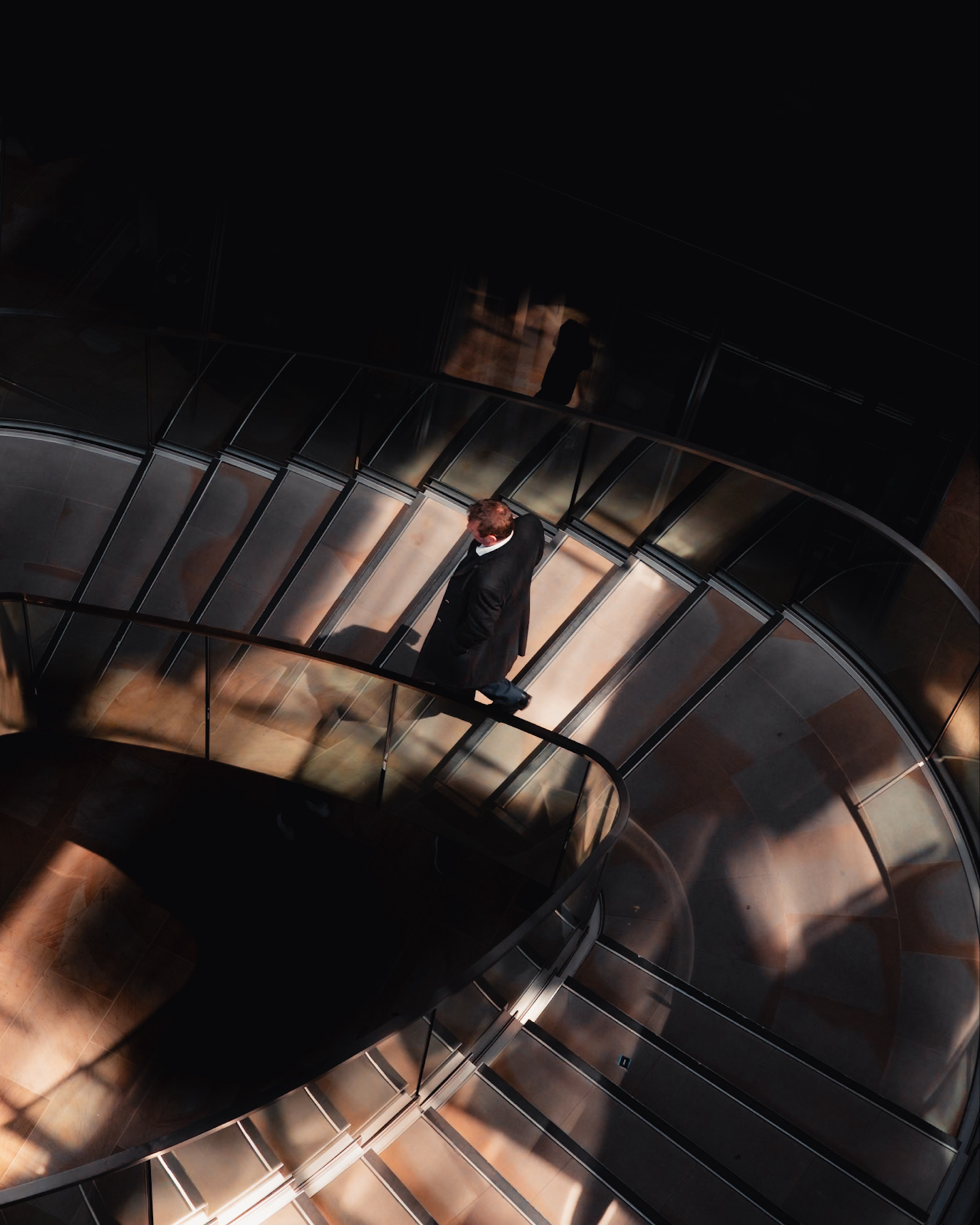 A man going entering a small amount of light whilst going down a dark staircase shot from above 
